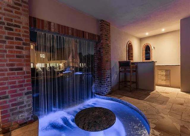Waterfall feature with blue lighting in an outdoor area, by a brick wall, next to a bar.