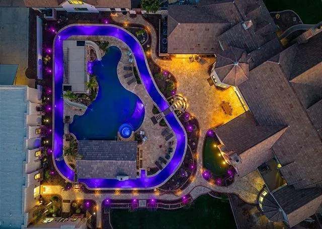 Aerial view of a luxury backyard with a pool, lazy river with purple lights, and patio at dusk.