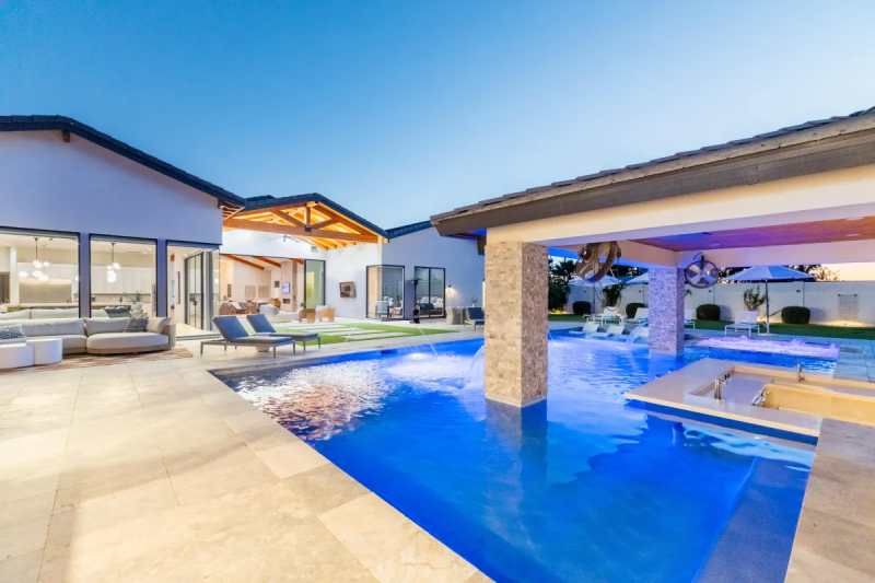 Luxury backyard with a blue swimming pool, poolside bar, and a modern home.