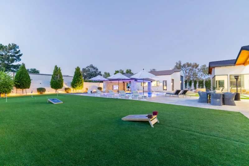 Backyard with pool, lawn, and games like cornhole at dusk.