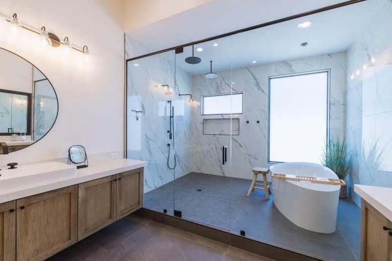 Modern bathroom with glass shower, white tub, and wood vanity.