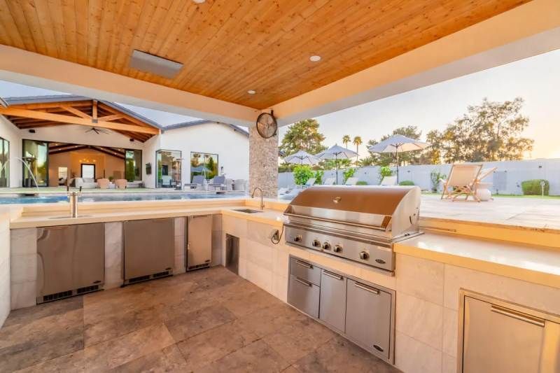 Outdoor kitchen with stainless steel grill, cabinets, and a view of a pool.