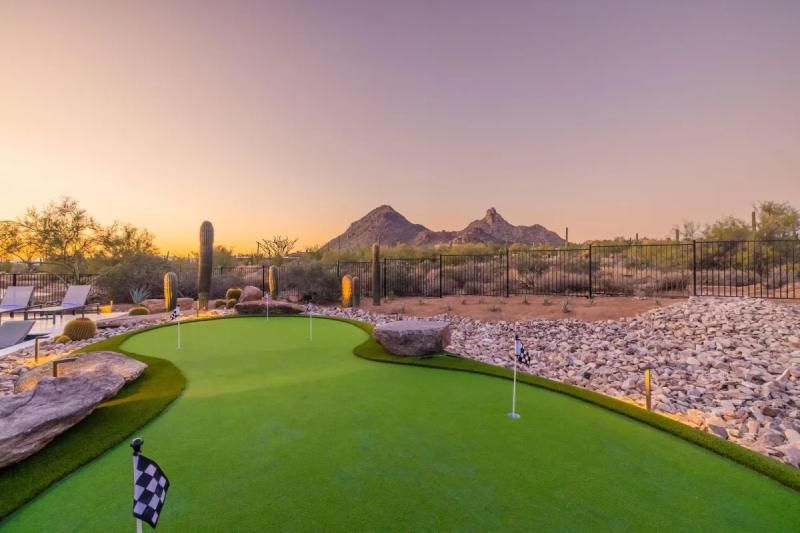 A putting green in a desert landscape at sunset, with flags and a mountain backdrop.