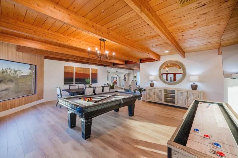 Game room with pool table, shuffleboard, and wood-beam ceiling. White walls and wood accents.