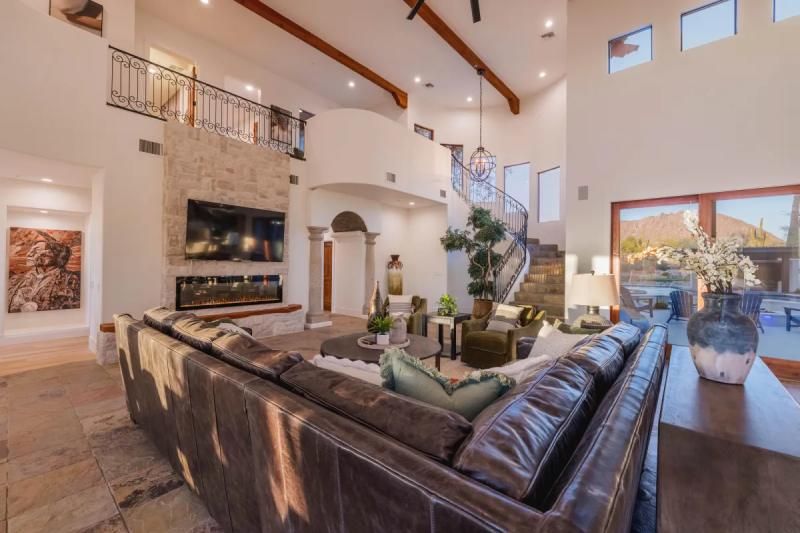 Spacious living room with a leather couch, stone fireplace, and a winding staircase.