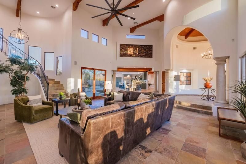Spacious living room with high ceilings, leather sofa, and a staircase. Light-filled with an arched doorway and large windows.