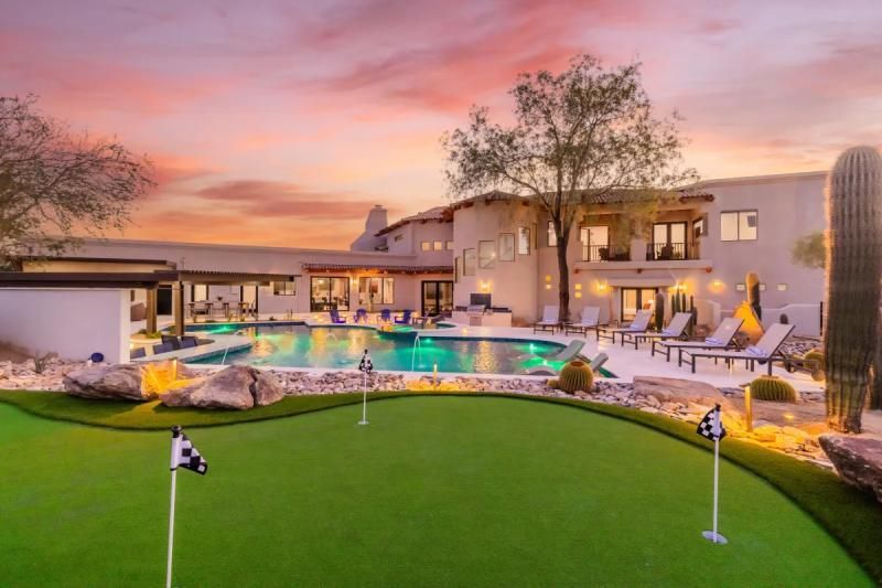 Luxury home with pool, putting green, and sunset sky.