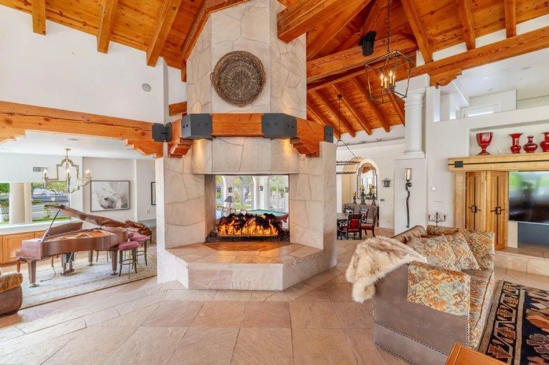 Grand living room with a large stone fireplace, piano, and wooden beam ceiling.