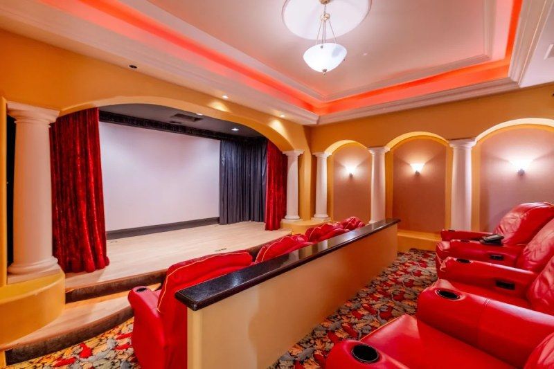 Home theater room with red leather seating, a large screen, and decorative arches; gold and red decor.