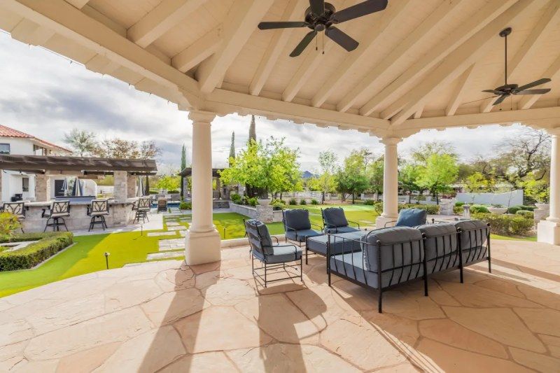 Patio with seating under a white-columned awning overlooking a backyard with a bar.