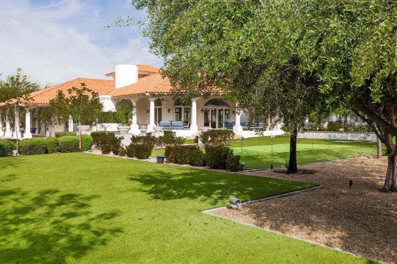 Large white house with terracotta roof, columns, and a grassy lawn under a sunny blue sky.