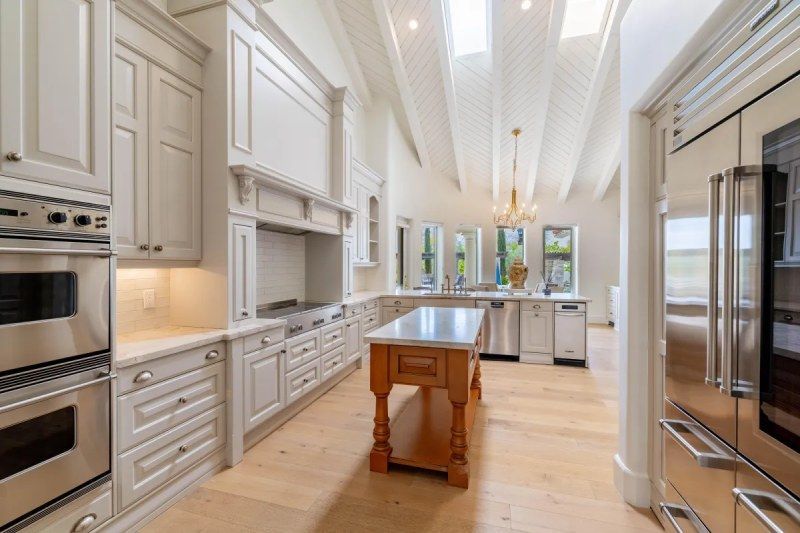 Elegant kitchen with light wood floor, white cabinets, and a wooden island.