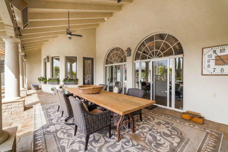 Covered patio with dining table, rug, arched windows, and a clock.