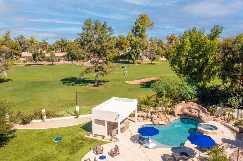 Backyard pool with golf course view, blue umbrellas, white cabana. People golfing in the background.