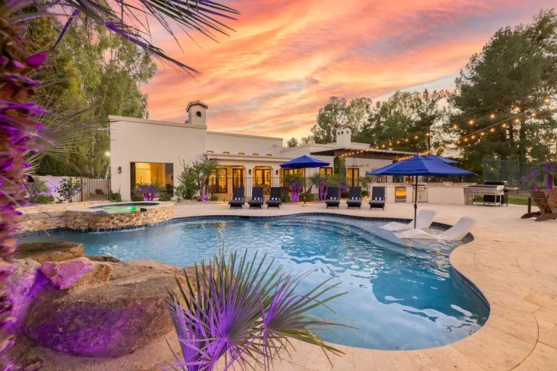 Luxury home with a pool at sunset. The sky is colorful, and the pool has lounge chairs.