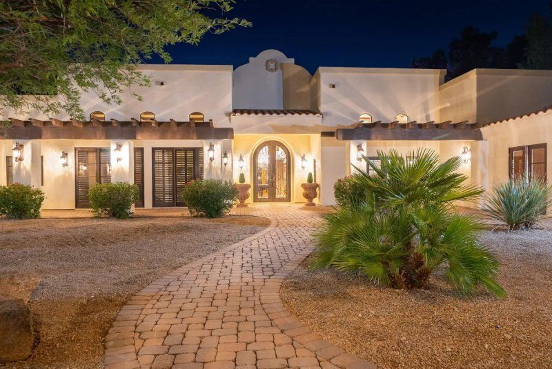 Night exterior of a stucco home with a brick pathway. Lights illuminate the entrance.