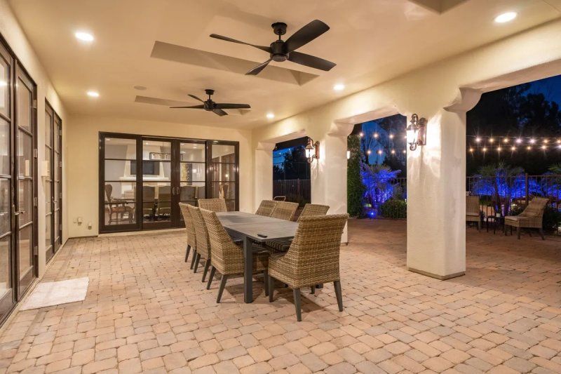 Patio with dining table and chairs, brick flooring, and string lights, at dusk.