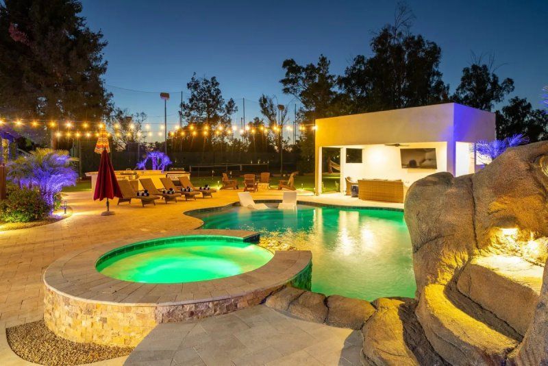 Nighttime view of a pool area with a spa, pool, and a poolside bar, all illuminated by string lights.