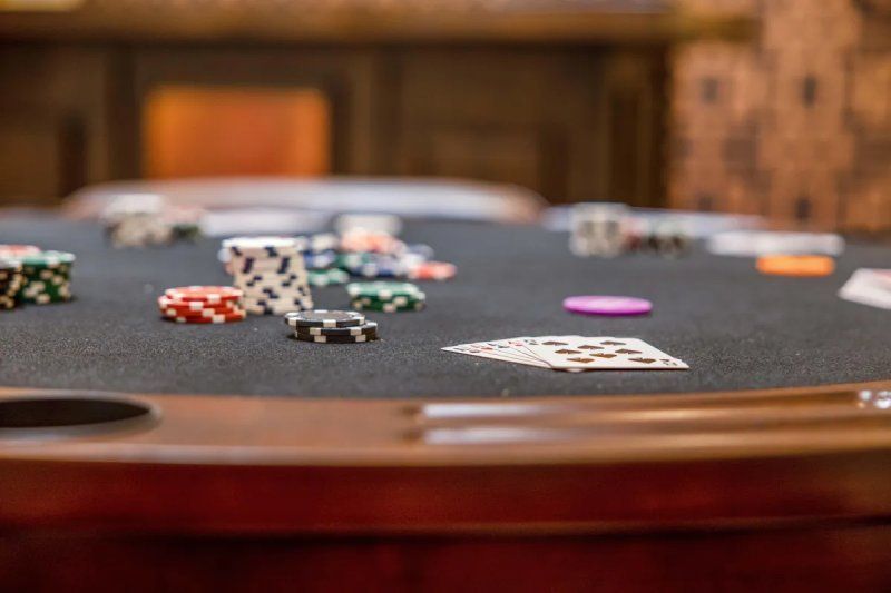Poker table with cards, chips, and a purple chip on a black felt surface, in a wooden-paneled room.