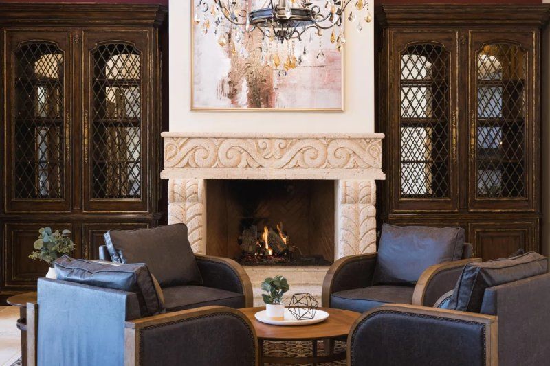 Cozy living room with fireplace, dark wood cabinets, and leather armchairs arranged around a round coffee table.