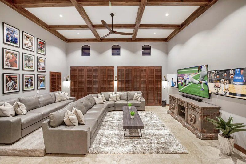 Spacious living room with gray sectional sofa, multiple TVs, wooden beams, and framed photos.