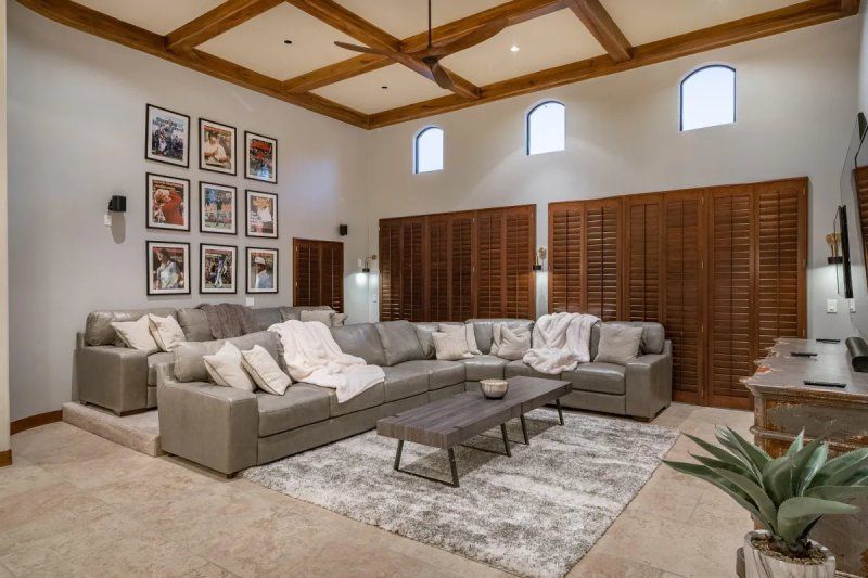 Large home theater with sectional sofa, rug, and artwork. Wooden ceiling beams and shutters.