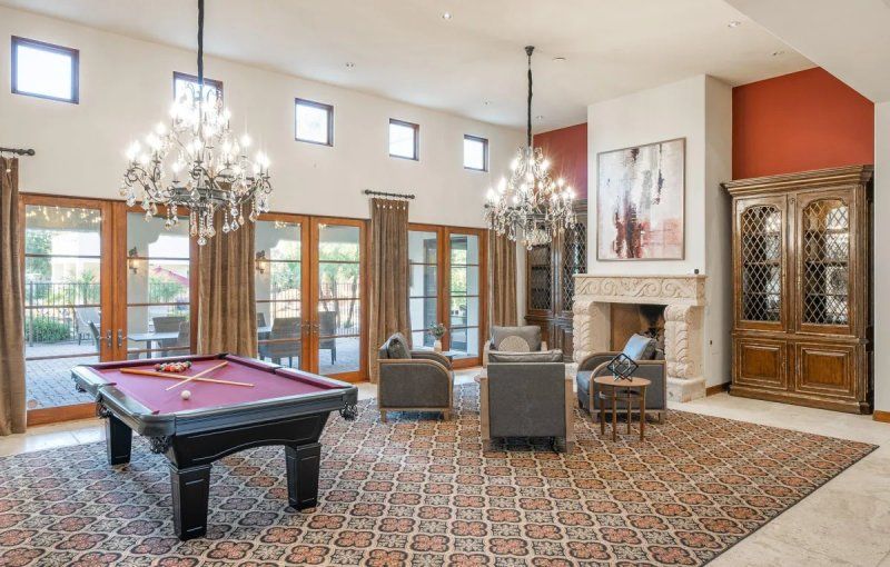 Spacious game room with pool table, armchairs, and two chandeliers; french doors lead to an outdoor patio.
