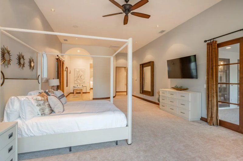 Spacious bedroom with a four-poster bed, white dresser, large mirror, TV, and access to an outdoor area.