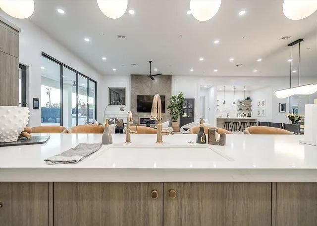 Modern kitchen interior with white countertops, gold faucet, and open view to living area.
