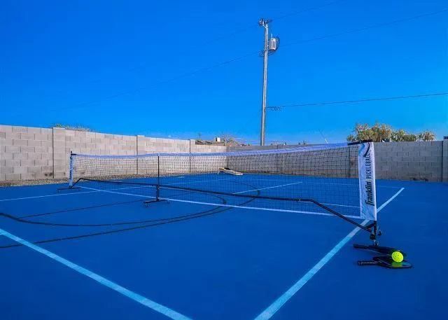 Blue pickleball court with net, ball, and paddle; blue sky background.