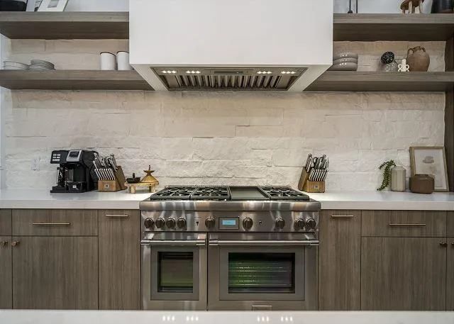 Stainless steel range in a modern kitchen with wooden cabinets and open shelves.