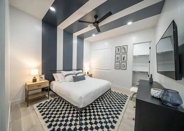 Modern bedroom with black and white accents: bed, dresser, rug, ceiling stripes.