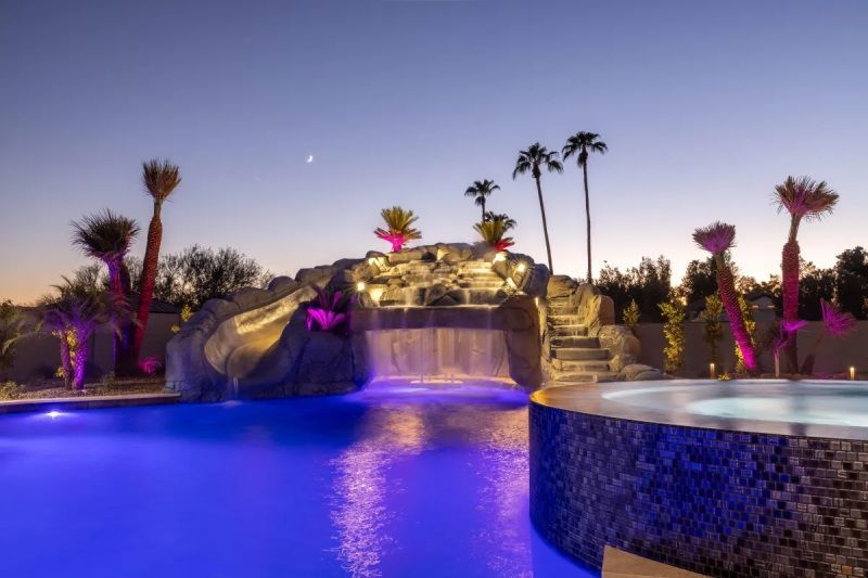 Pool at dusk with waterfall and illuminated palm trees.