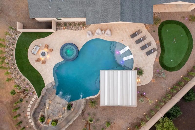 Aerial view of a backyard with a pool, putting green, patio, and seating areas.