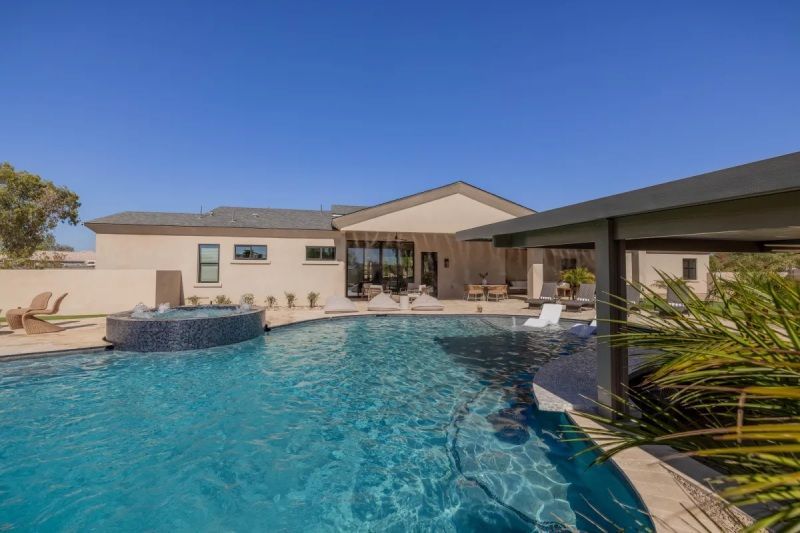 Backyard with pool, jacuzzi, and covered patio on a sunny day.