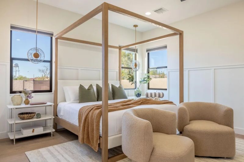 Bedroom with a canopy bed, two armchairs, white walls, and large windows.