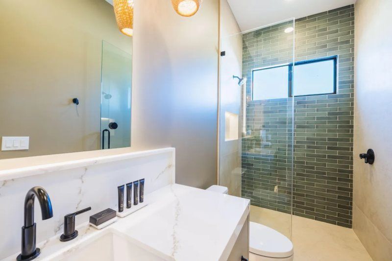 Modern bathroom with marble countertop, black faucet, glass shower, and green tile wall.