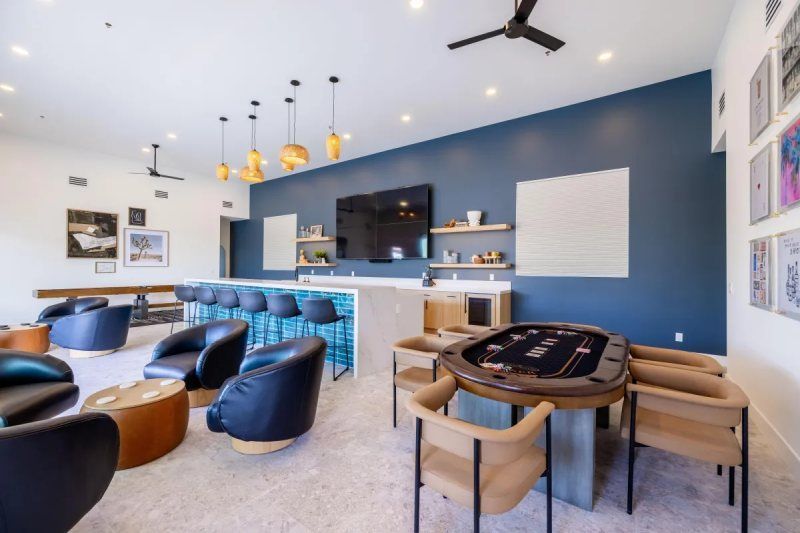 Lounge area with bar, poker table, and seating. Blue accent wall, pendant lights, and modern decor.