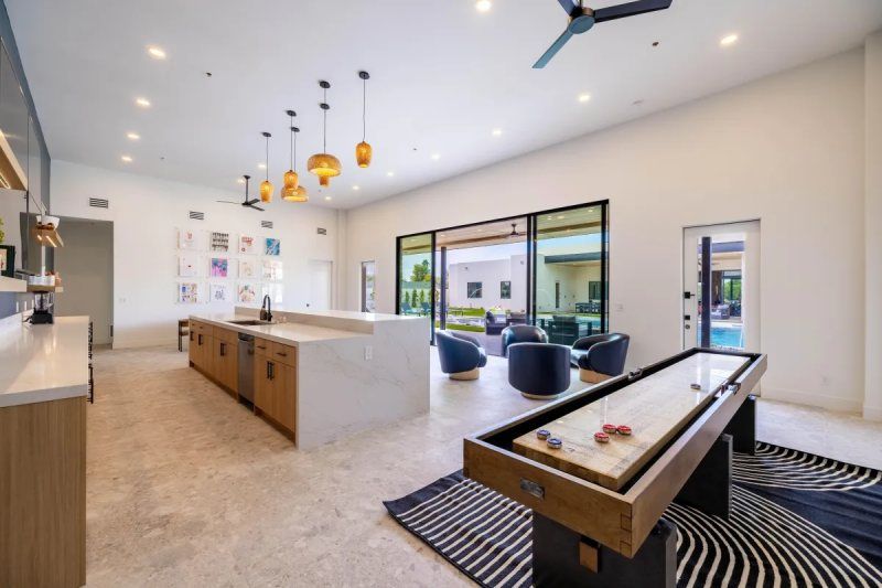 Interior of a modern rec room with shuffleboard, kitchen island, seating, and patio access.