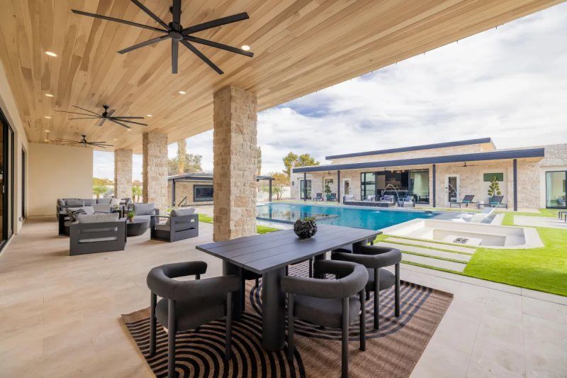 Patio with dining table and chairs overlooking a pool, grassy yard, and modern home.