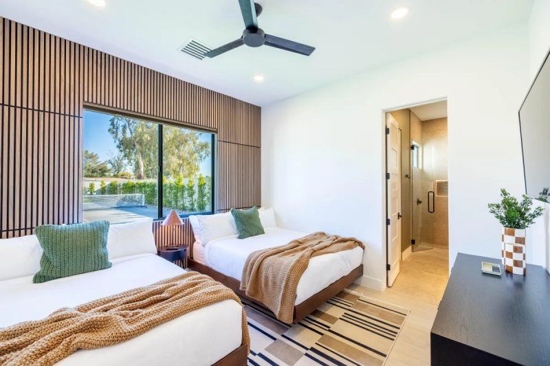Bedroom with two beds, window with view, wooden accent wall, doorway to bathroom.