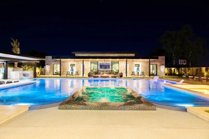 Night view of a luxurious swimming pool with illuminated water and a modern house in the background.