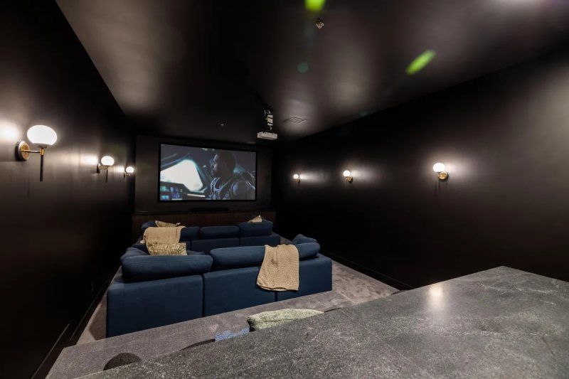 Dark home theater with blue sectional sofa, projector screen, and wall sconces.
