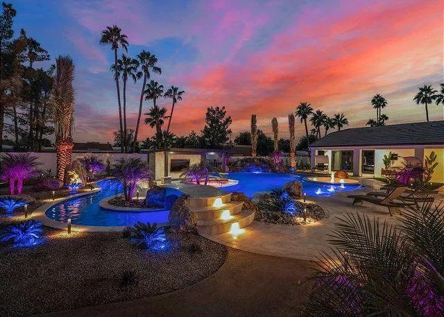 Pool area at sunset, with palm trees, water features, and colorful lighting.