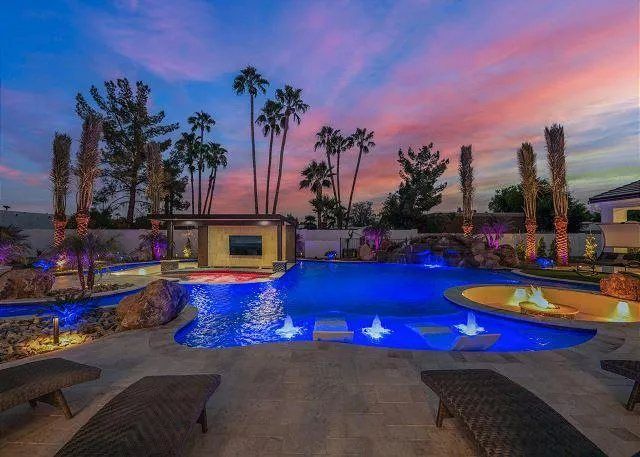 Pool at dusk with blue lights, palm trees, and colorful sky. Loungers are in the foreground.