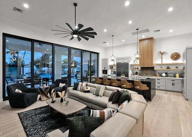 Open-concept living space with a large sectional sofa, kitchen island with seating, and floor-to-ceiling glass doors overlooking a patio.