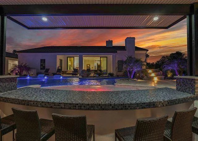 Bar overlooking a pool with house in the background at sunset.