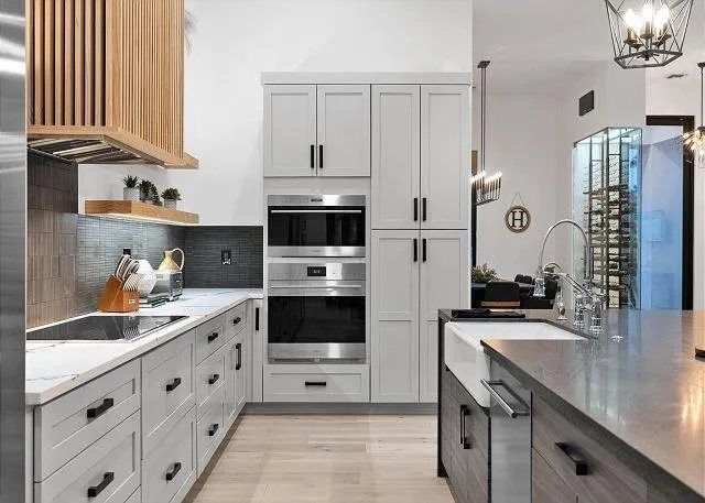 Modern kitchen with light gray cabinets, stainless steel appliances, and wood accents.