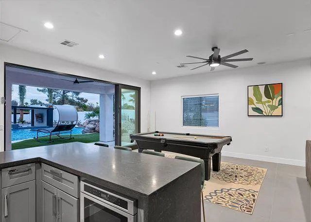 Indoor entertainment room with pool table, kitchen counter, and view of a pool.
