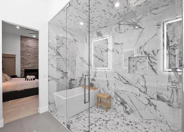 Bathroom with marble shower and tub, glass door. Bedroom visible in doorway.